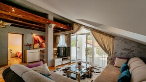 Una sala moderna con un sofá, una mesa de centro de vidrio y un televisor. Hay un balcón con vistas al exterior.