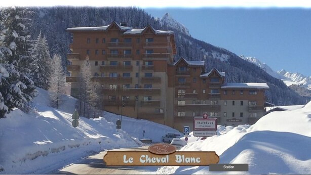 A multi-story hotel with a sign reading "Le Cheval Blanc" in a snowy mountainous area. - Beautiful 4-room apartment in VALFREJUS (VALFREJUS)