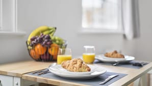 En frukostuppdukning med croissanter på tallrikar, en fruktskål och ett glas apelsinjuice.