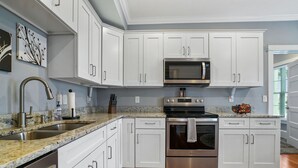 Una cocina moderna con armarios blancos, electrodomésticos de acero inoxidable, encimeras de granito y piso de madera.