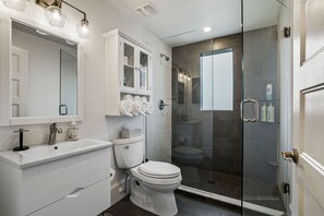 A modern bathroom with a glass-enclosed shower, a white sink, and a toilet.