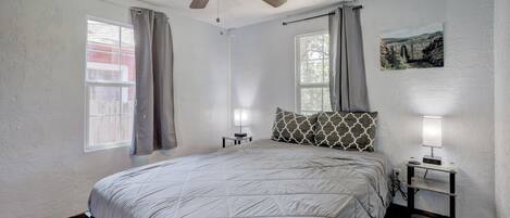A bedroom with a bed, a ceiling fan, a nightstand with a lamp, and a painting on the wall.