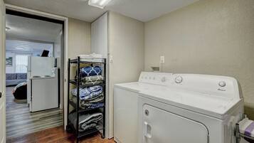 A laundry room with a white washer and dryer, a shelf with folded towels, and a door leading to a bedroom.
