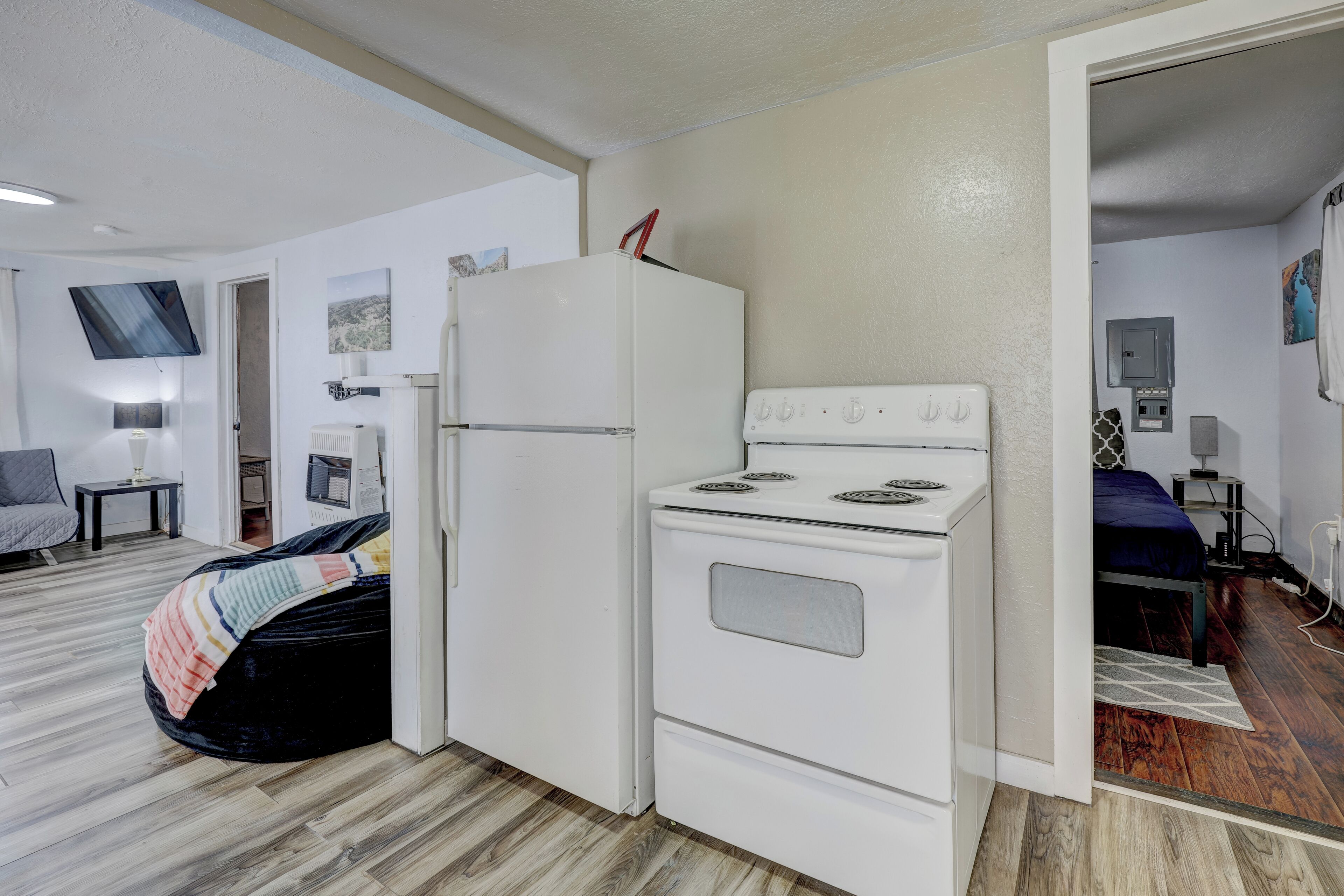 A compact kitchen with a white refrigerator, stove, and microwave. A bean bag chair is visible in the living area.