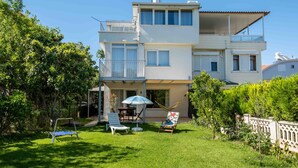 A two-story building with a balcony, a covered patio, and a grassy backyard with a hammock, chairs, and a table. - Villa Belinda (Serik)