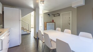 A modern kitchen with white cabinets, a built-in oven, and a stainless steel range hood. There is a dining area with a white table and chairs, and a staircase leading to another level. - Villa Belinda (Serik)