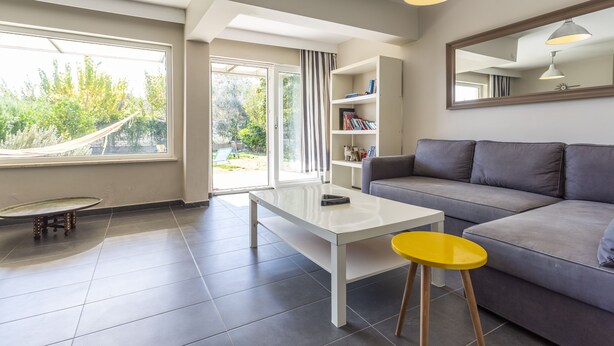 A modern living room with a sofa, a white table, a yellow stool, and a bookshelf. - Villa Belinda (Serik)