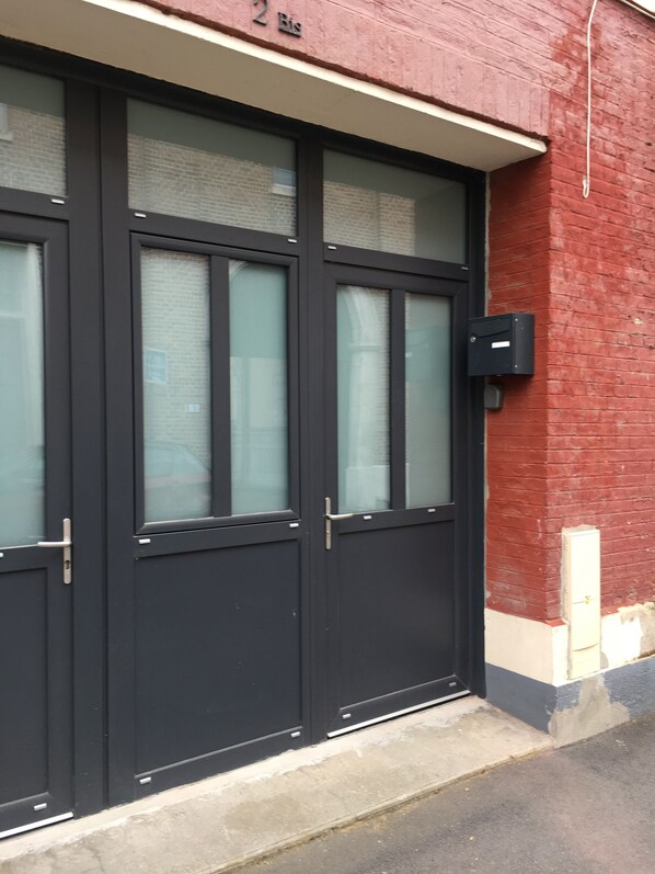A black double door with a glass panel, a mailbox, and a brick wall. - T1 Idéalement Situé Hyper Centre/canal Plus (amiens)