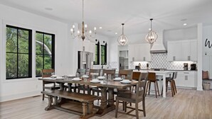 Una cocina amplia con una mesa de comedor grande, armarios blancos e iluminación colgante.
