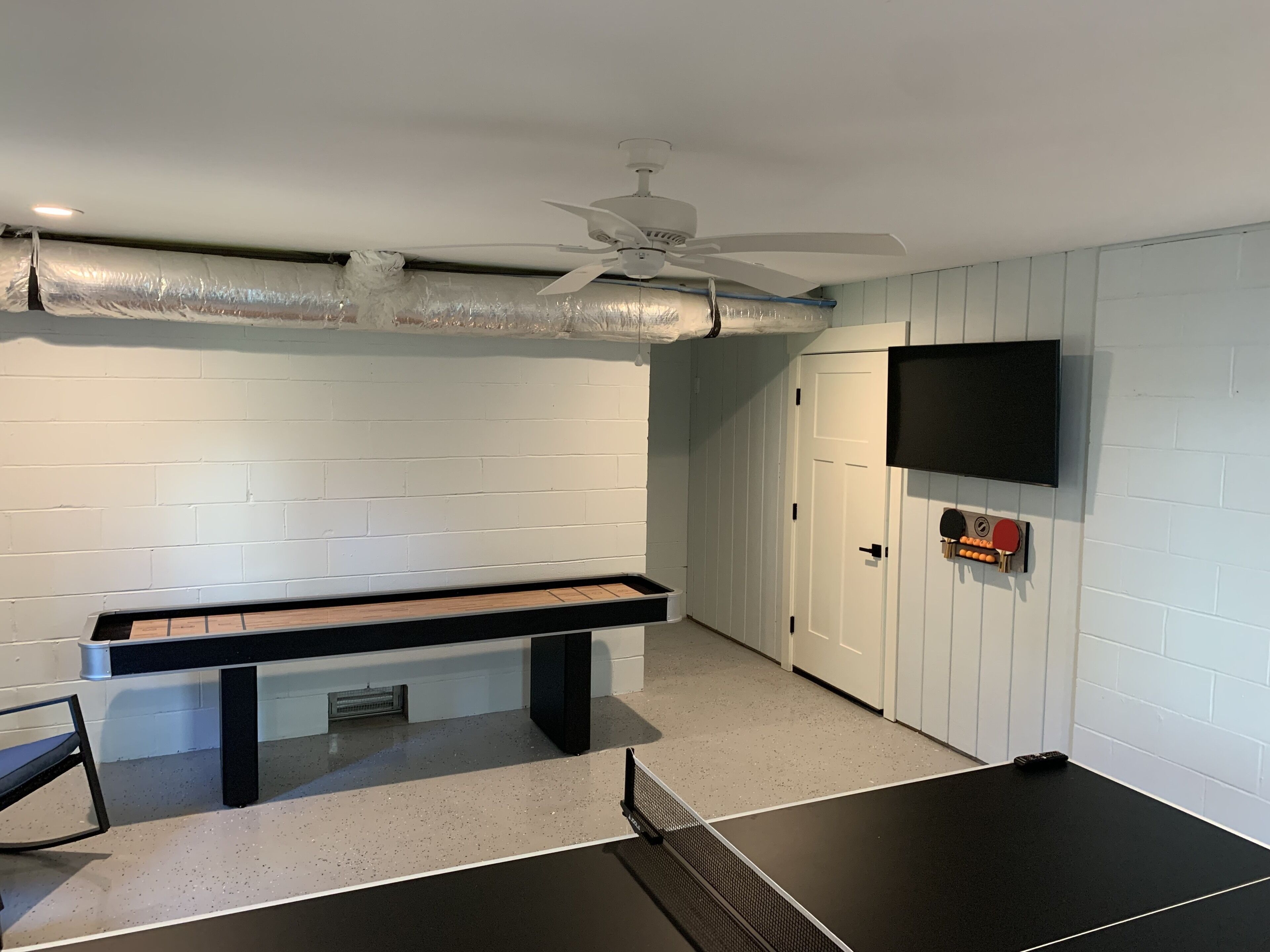 Una habitación con mesa de ping pong, ventilador de techo y televisor montado.