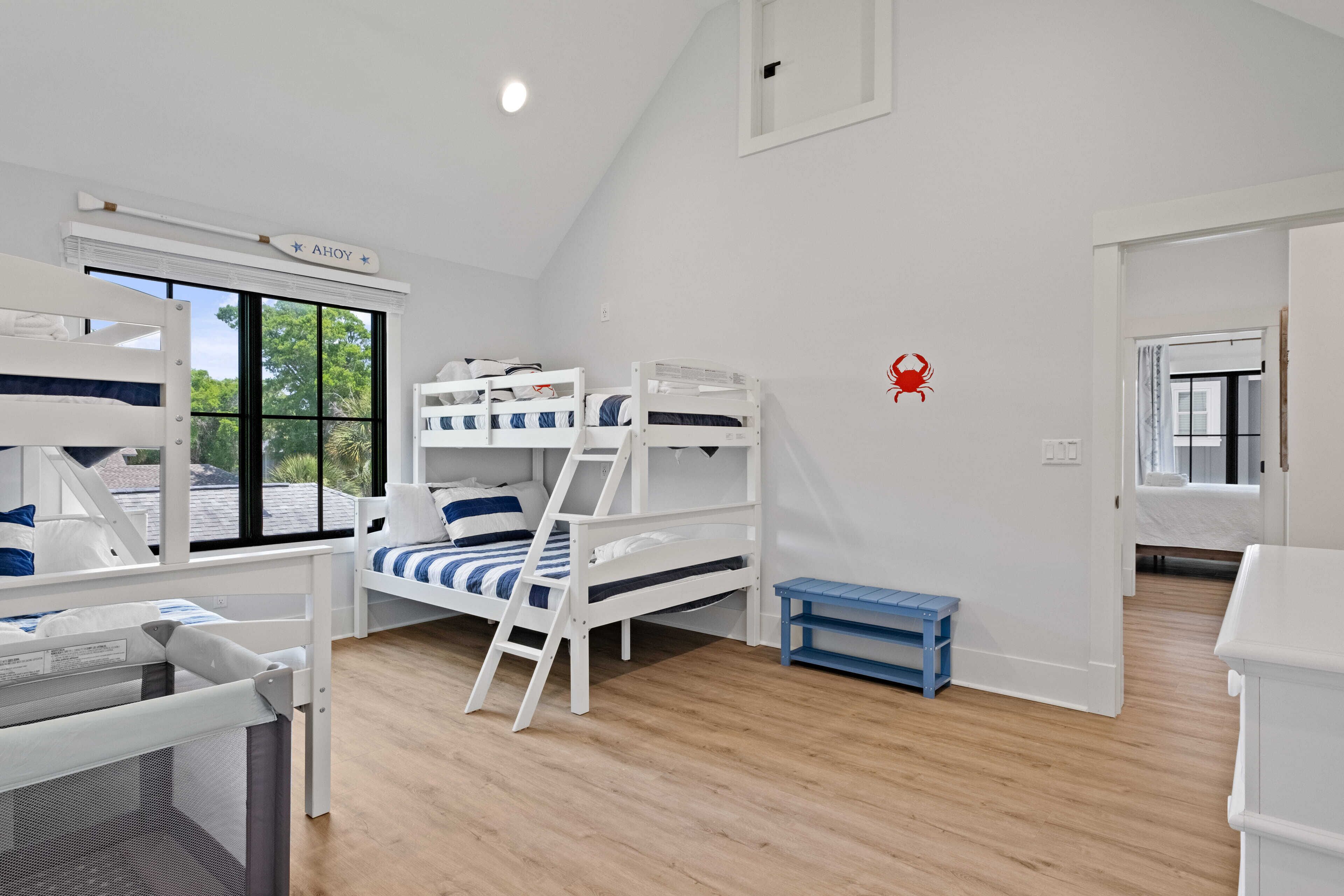 Ein Kinderzimmer mit Etagenbetten, einem kleinen blauen Tisch und einem Fenster mit Blick auf Bäume.