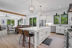 Une cuisine moderne avec des meubles blancs, un grand îlot central et des luminaires suspendus.