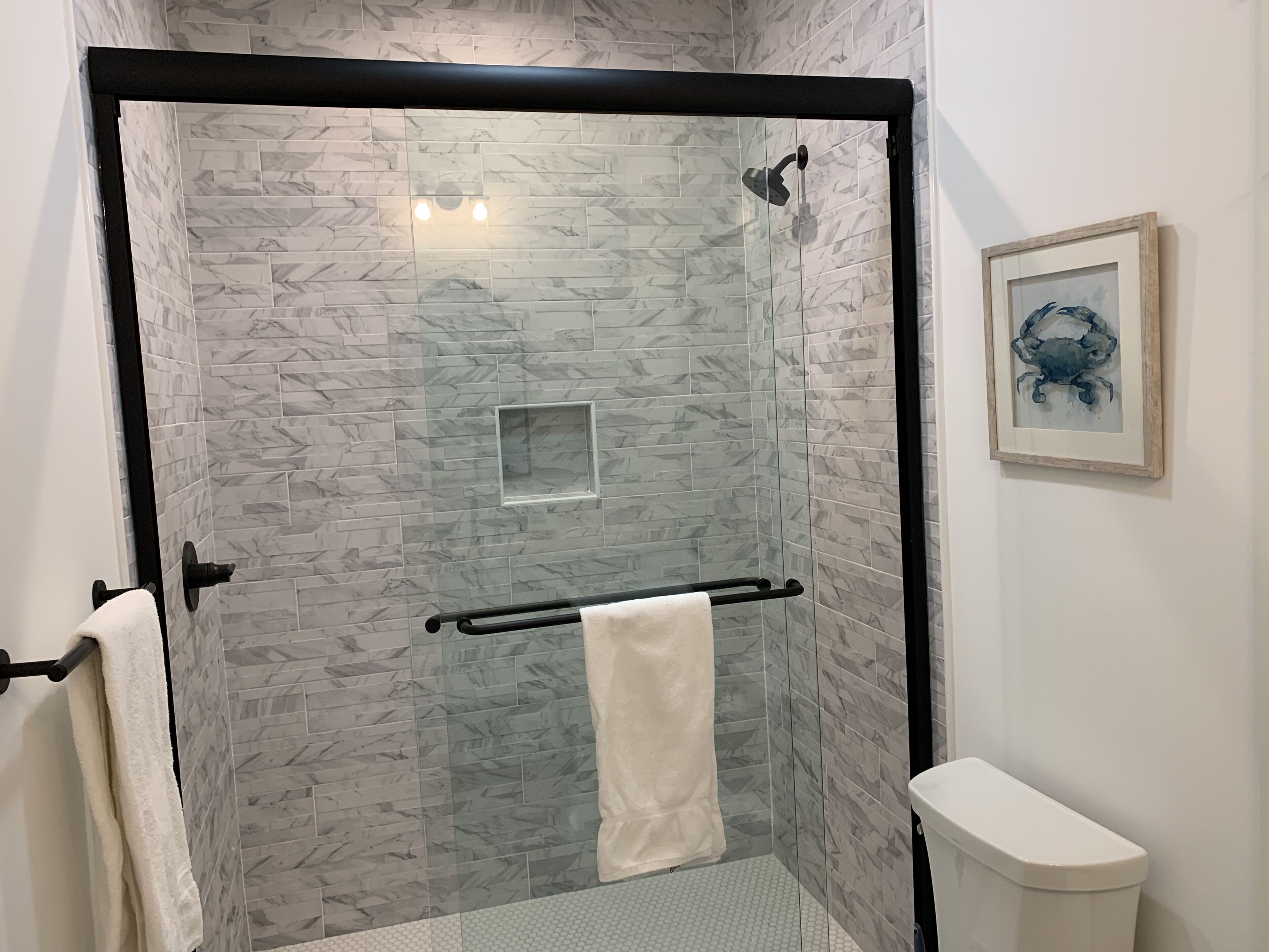 A glass-enclosed shower with a marble-patterned wall, a towel rack, and a framed artwork on the wall.