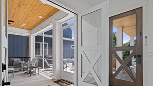 Un interior moderno con techo de madera, puerta de cristal con diseño geométrico y vistas a un área de estar exterior.