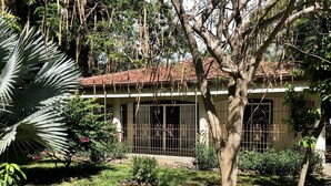 A house with a tiled roof, surrounded by a garden with various plants and a tree in the foreground. - Costa Rica Private Home with Swimming Pool . (Playa Hermosa)
