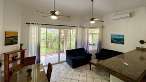 A spacious living area with two sofas, a dining table, and a kitchen area. There are ceiling fans, large windows with curtains, and artwork on the walls. - Costa Rica Private Home with Swimming Pool . (Playa Hermosa)