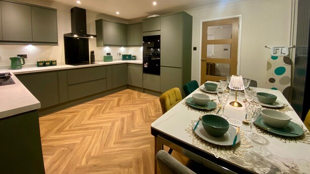 Una cucina moderna con mobili grigi, pavimento in legno a spina di pesce e zona pranzo con tavolo apparecchiato per quattro.