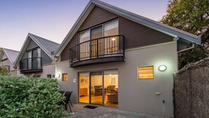 A modern two-story house with a balcony, large windows, and a well-lit interior.