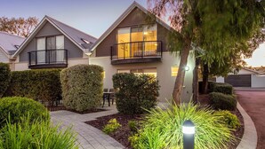 A modern two-story house with a balcony, a well-maintained garden, and a driveway.