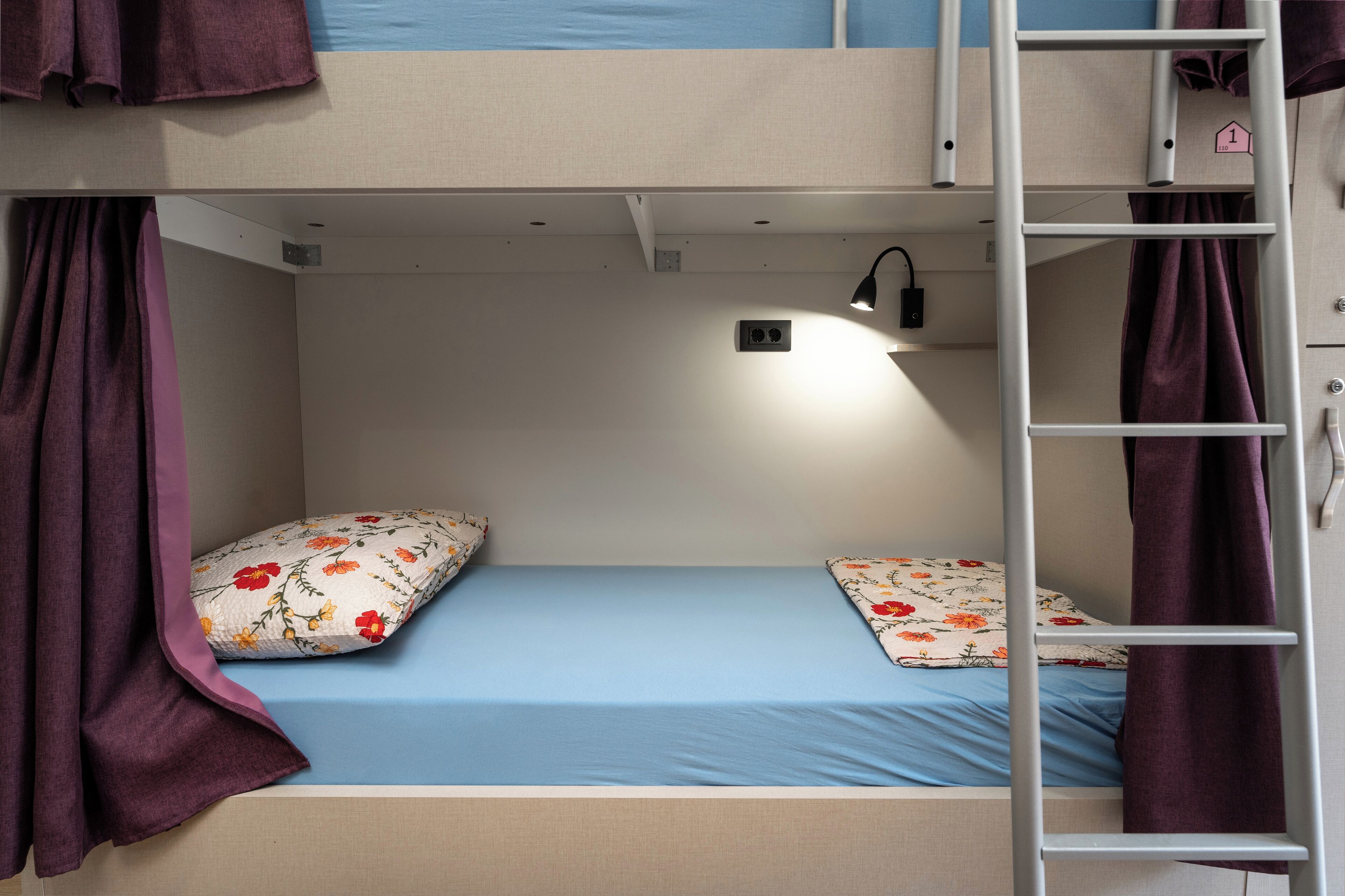 Una cama litera con escalera, un escritorio pequeño con lámpara y almohadas estampadas con motivos florales.
