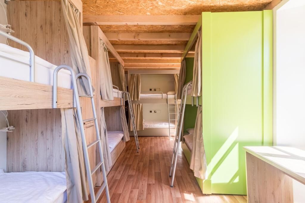 A dormitory room with bunk beds, wooden floors, and a green door.
