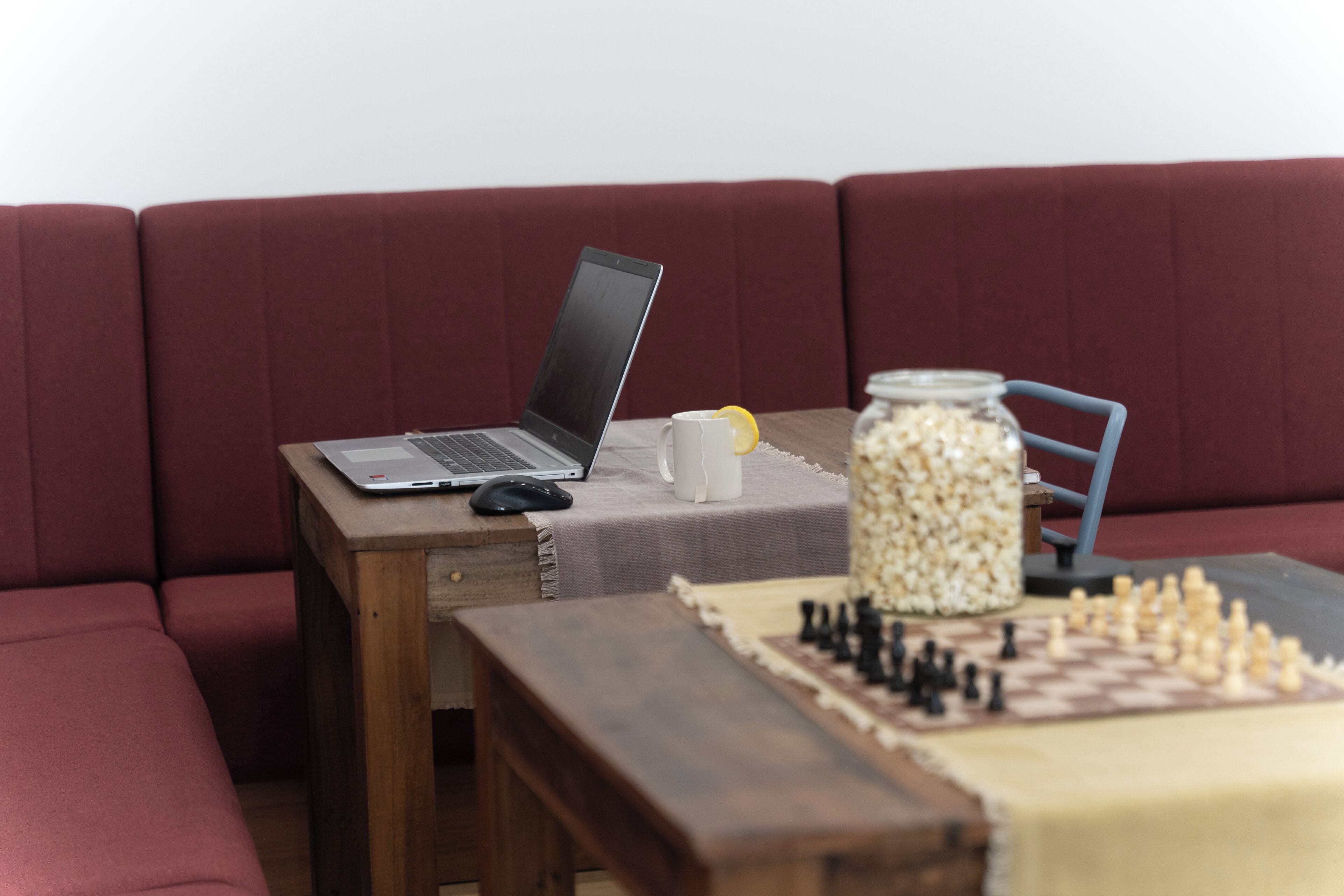 A laptop on a wooden table, a chessboard, and a jar of popcorn on a couch.