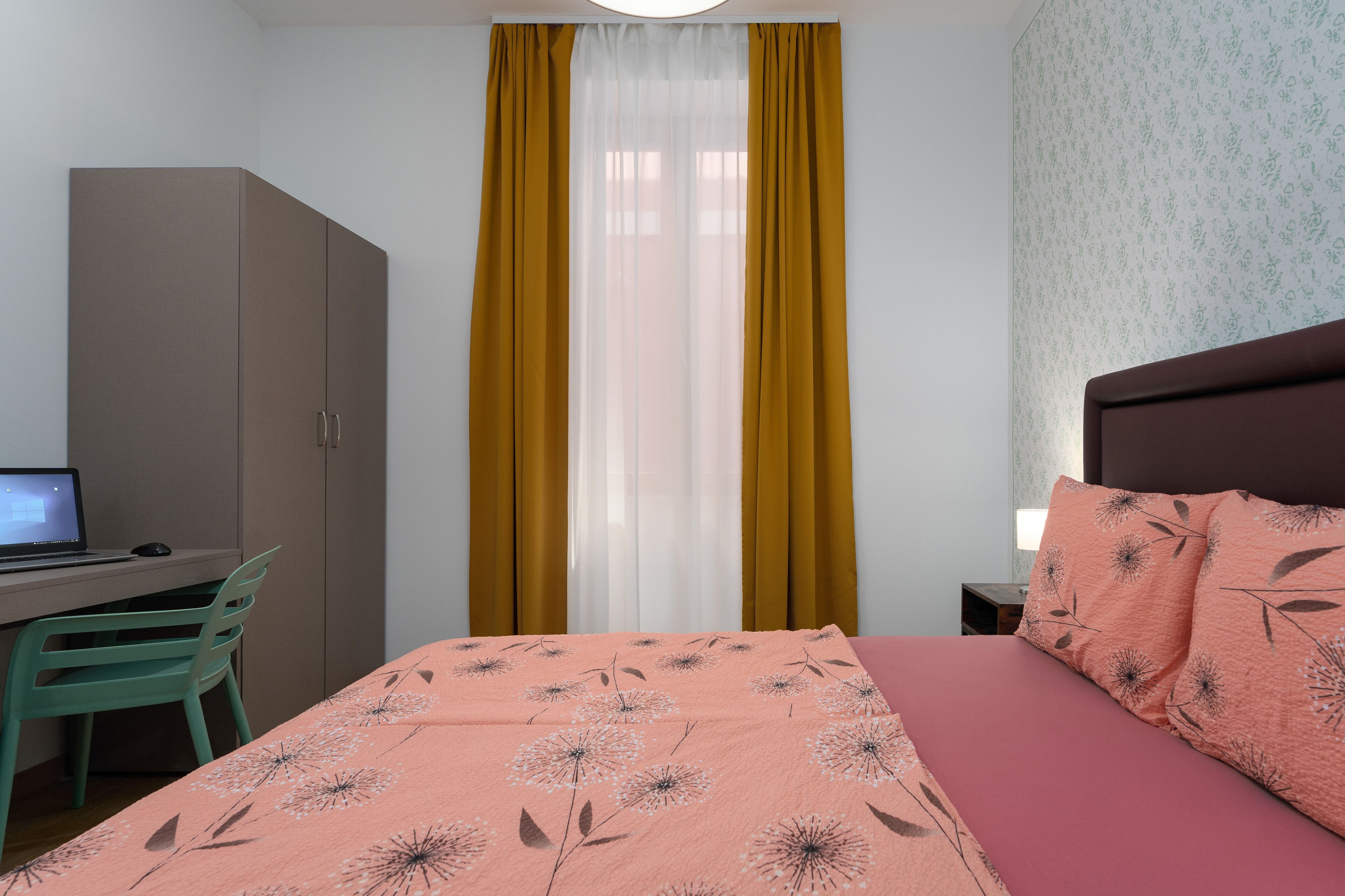 A bedroom with a bed, a desk with a computer, and a wardrobe.