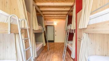 A narrow corridor with bunk beds on either side, wooden floors, and a red wall at the end.