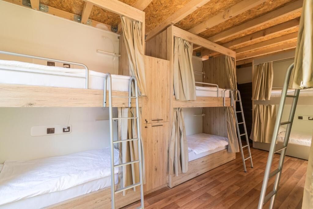 Une chambre avec des lits superposés, des poutres en bois, des échelles en métal et des rideaux.
