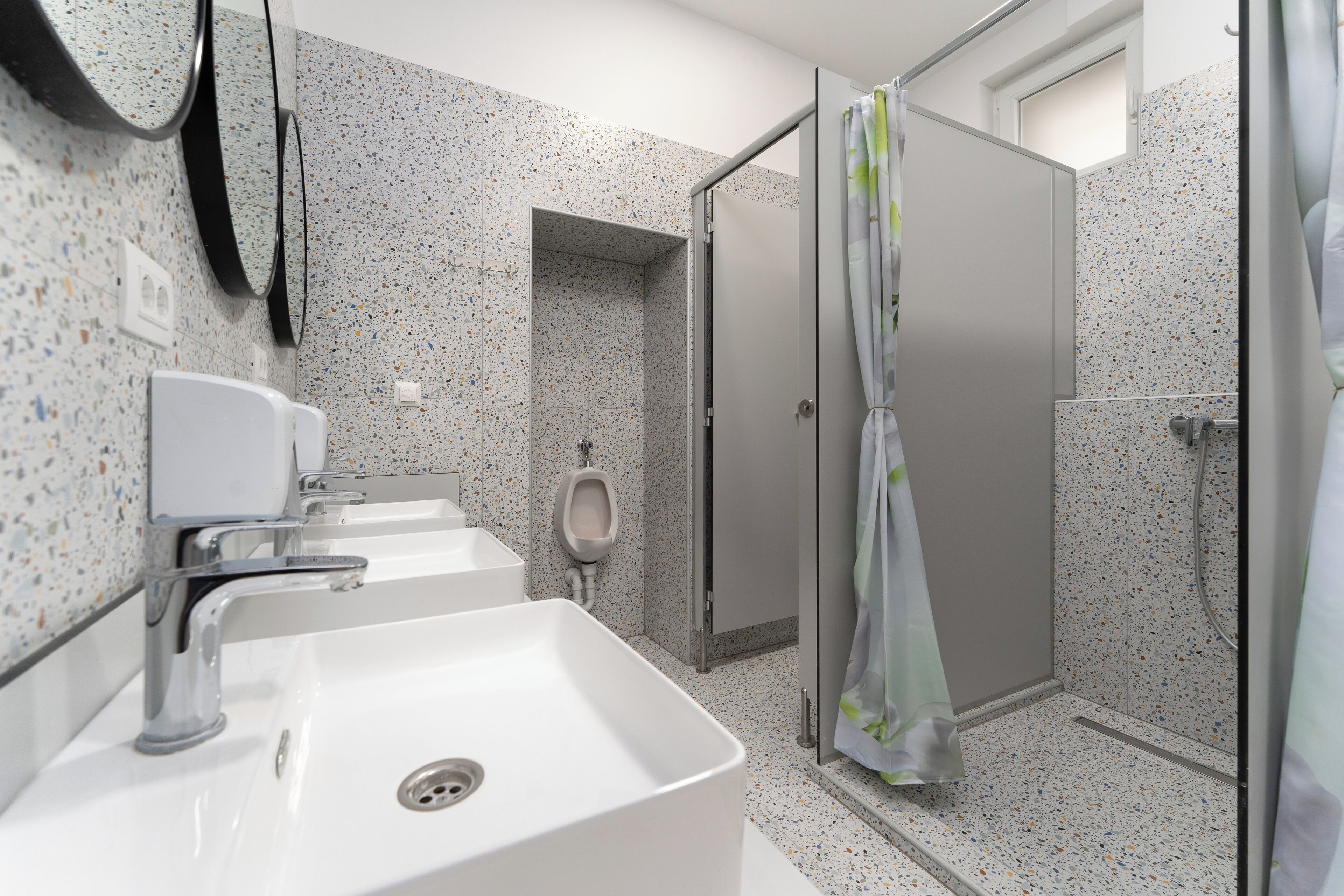A modern bathroom with a white sink, urinal, and shower stall.