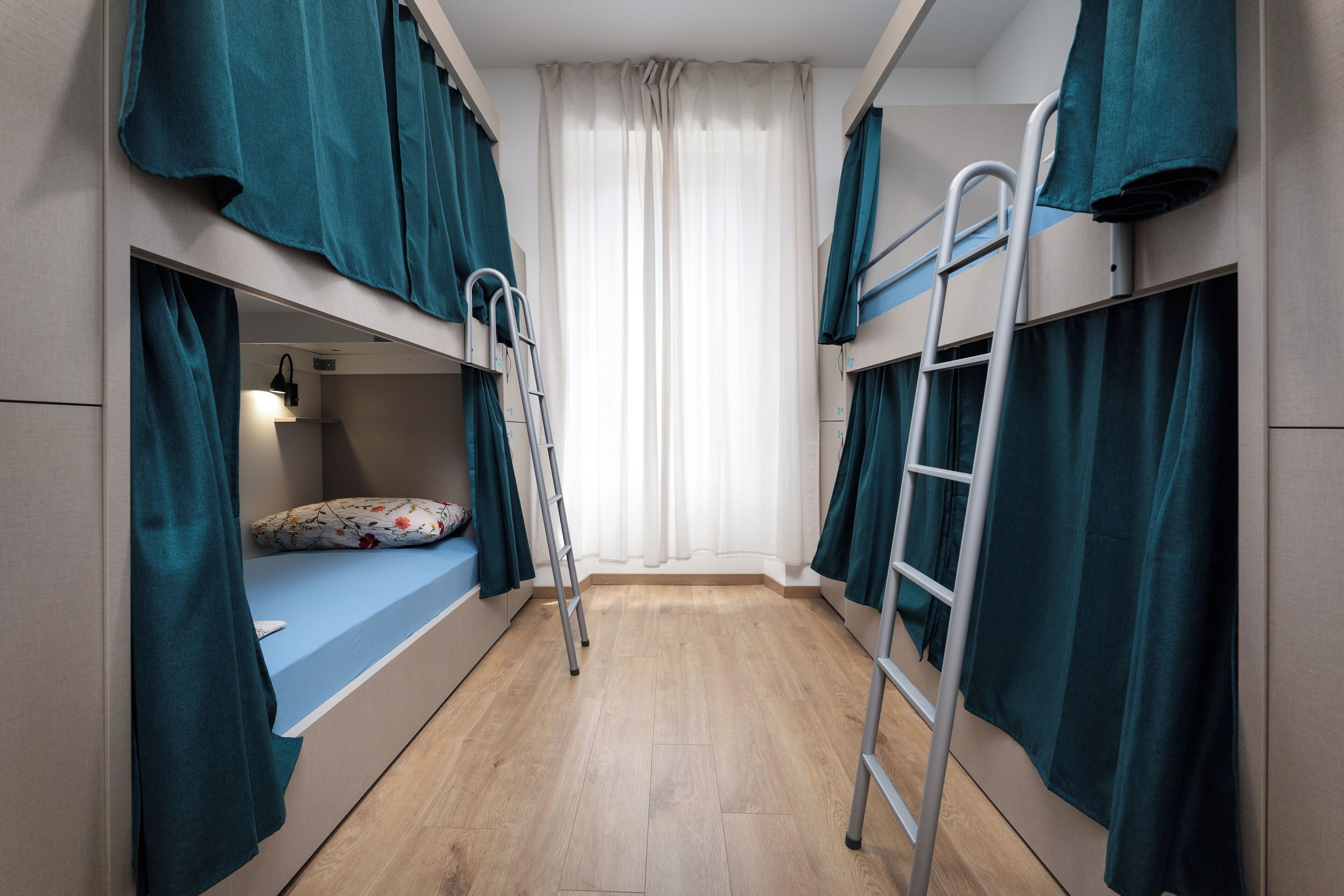 A bunk bed room with a wooden floor, a ladder, and teal curtains.