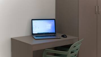 A laptop on a desk with a mouse, a green chair, and a cabinet in the background.