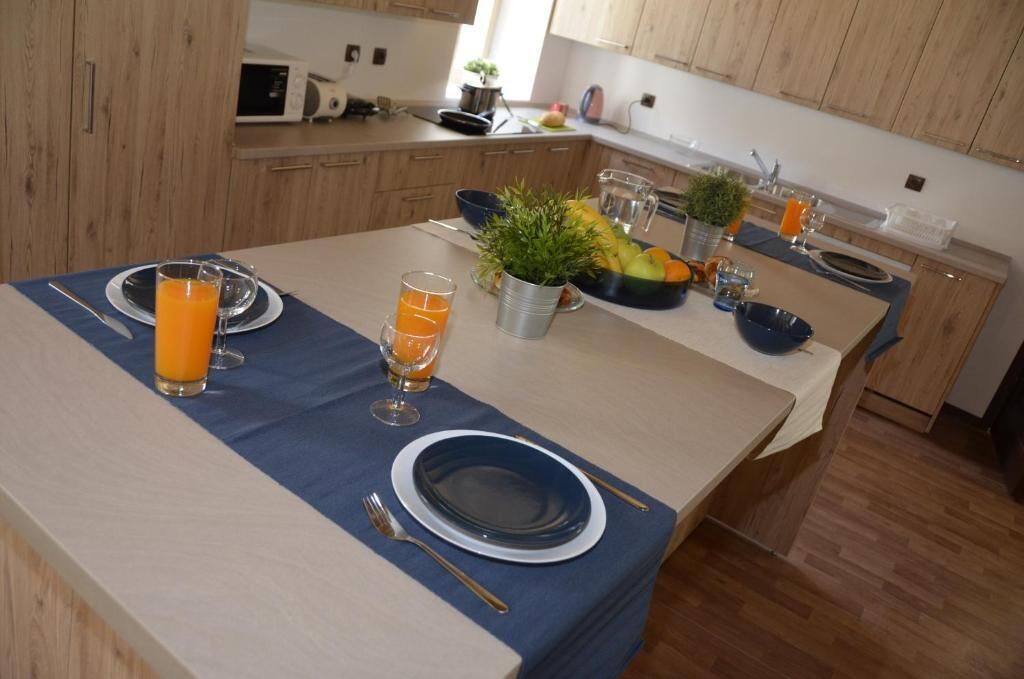 A dining area with a blue tablecloth, two plates, two glasses of orange juice, a fruit bowl, and a small potted plant.