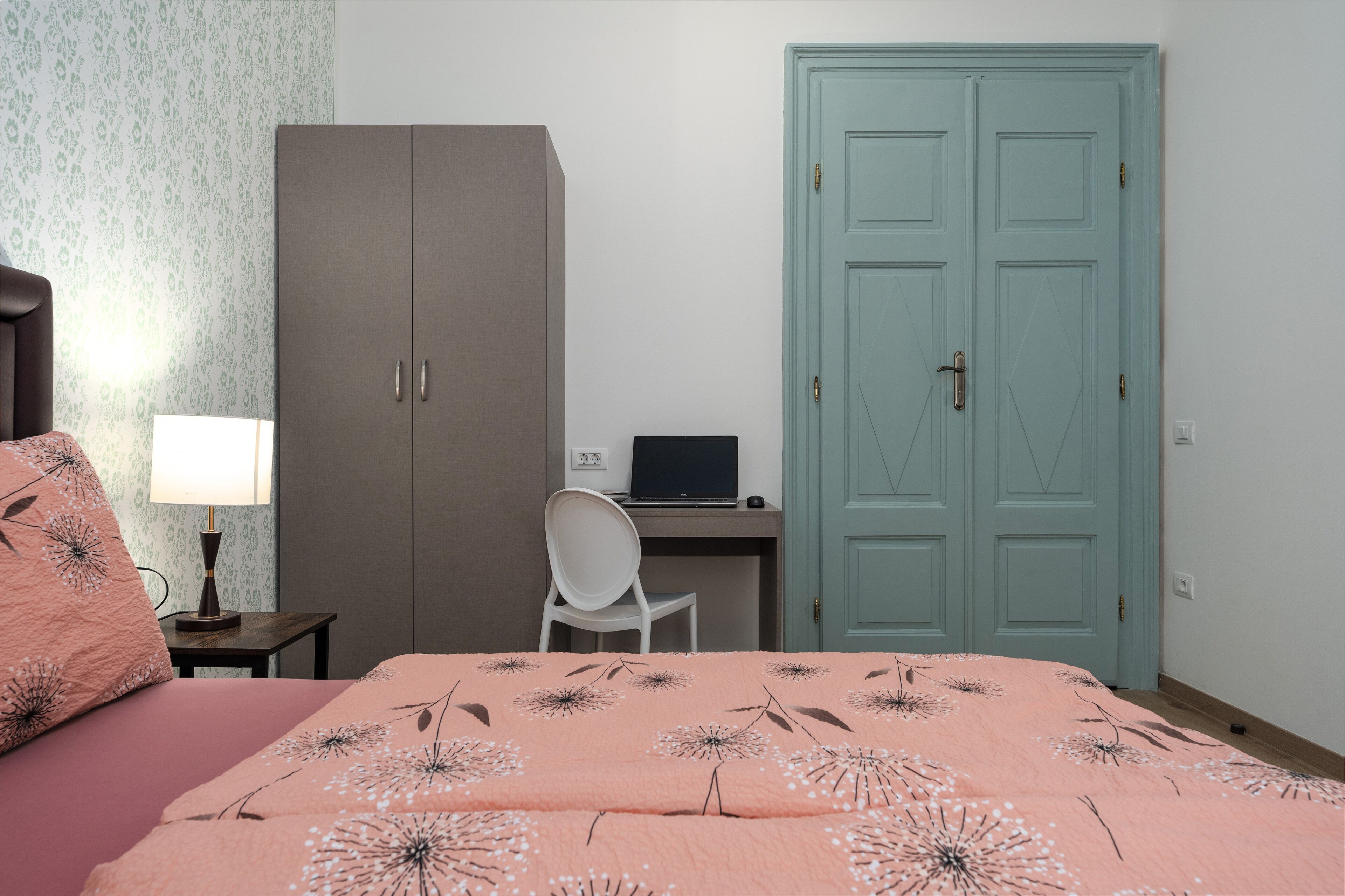 Une chambre à coucher avec un lit, un bureau avec un ordinateur portable, une armoire et une porte.