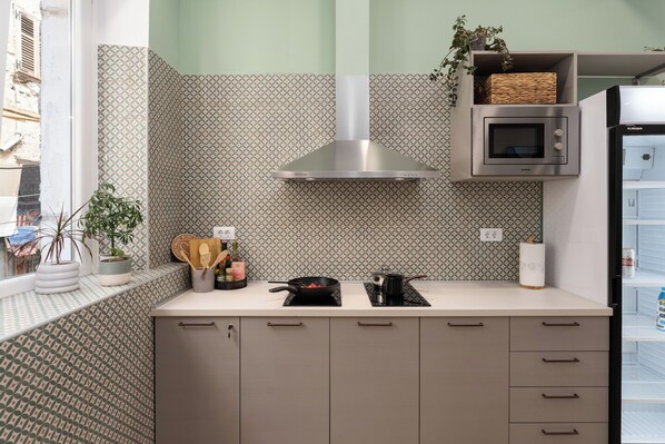 A modern kitchen with patterned backsplash, stainless steel range hood, microwave, and built-in shelves.