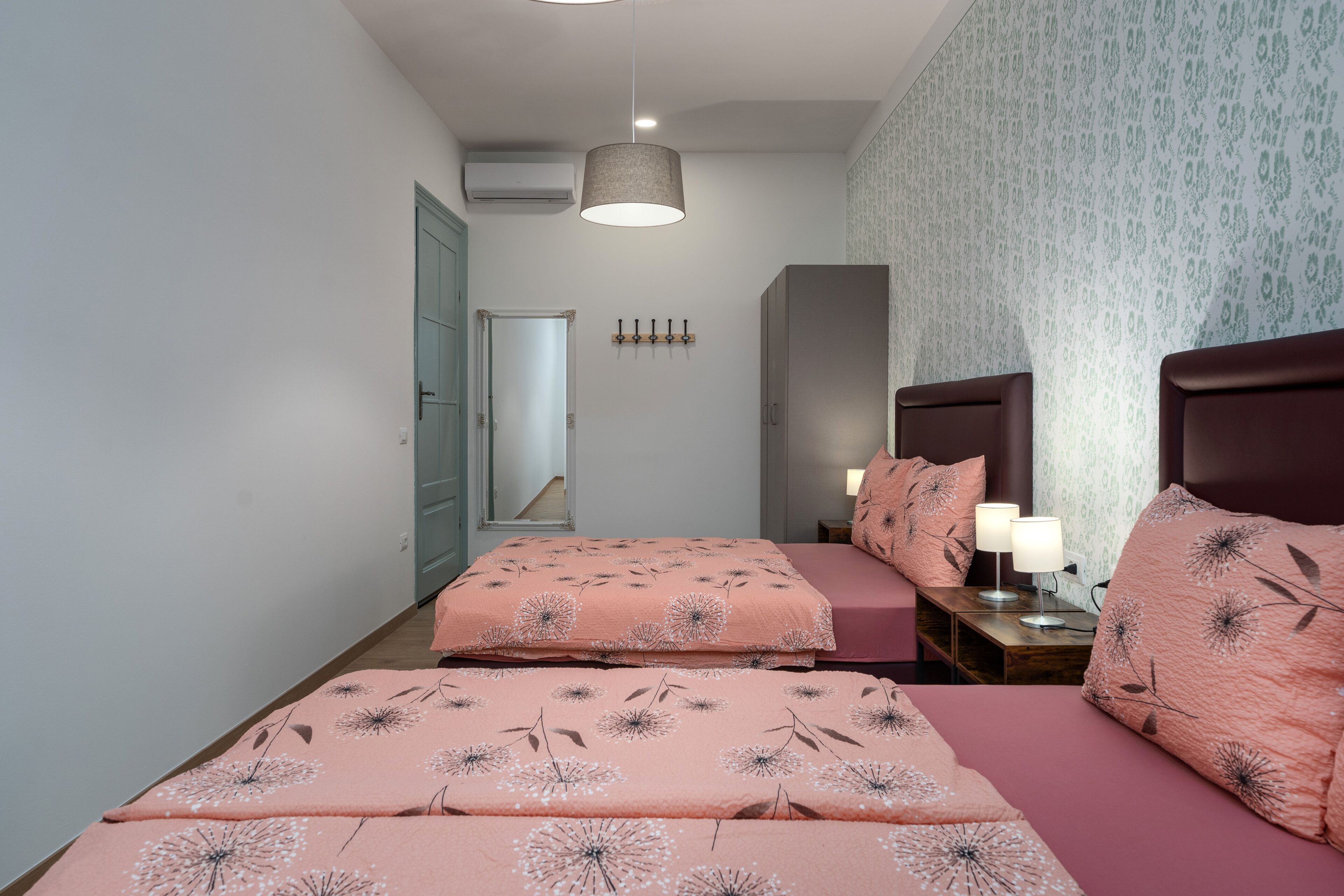 Une chambre avec deux lits, une table de chevet, un miroir et un luminaire fixé au mur.