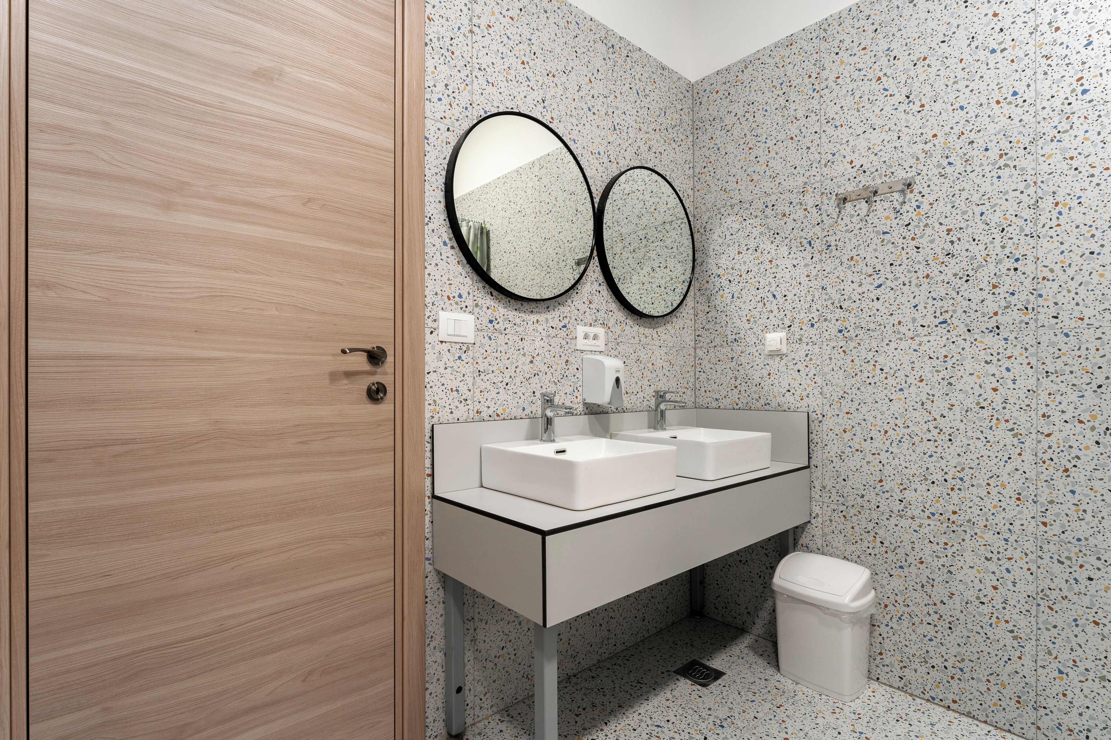 A modern bathroom with two sinks, a mirror, and a trash bin.