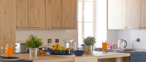 A modern kitchen with wooden cabinets, a central island with breakfast items, and a large window providing natural light.