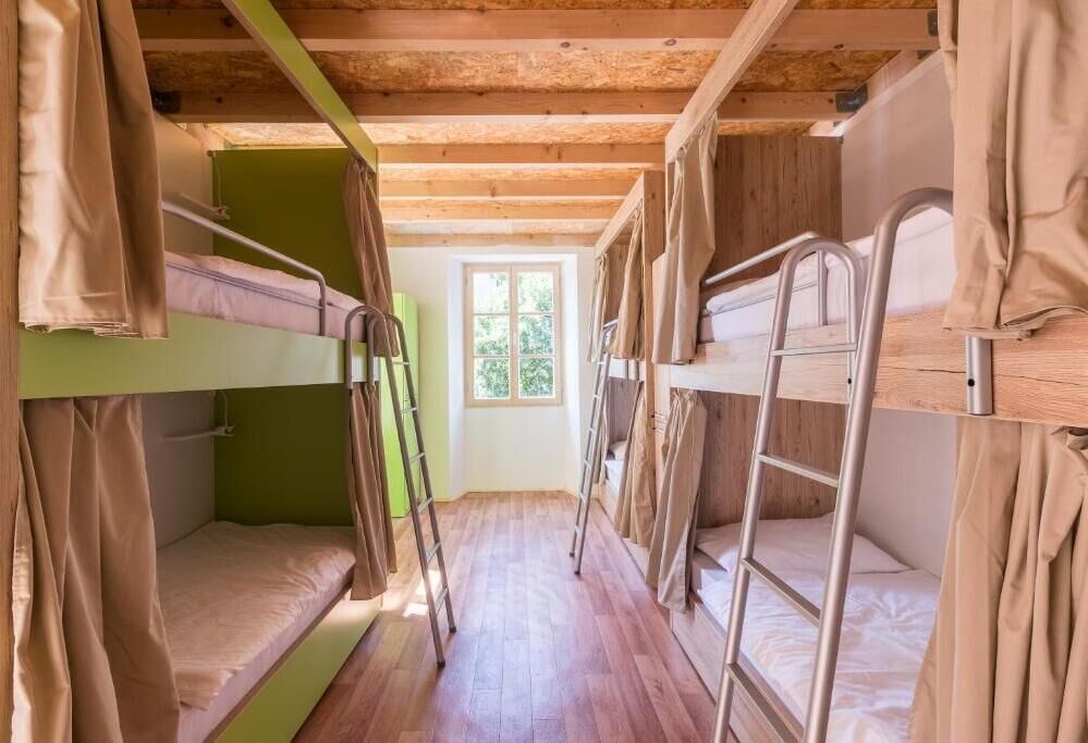 A narrow room with bunk beds, wooden beams, and a window.
