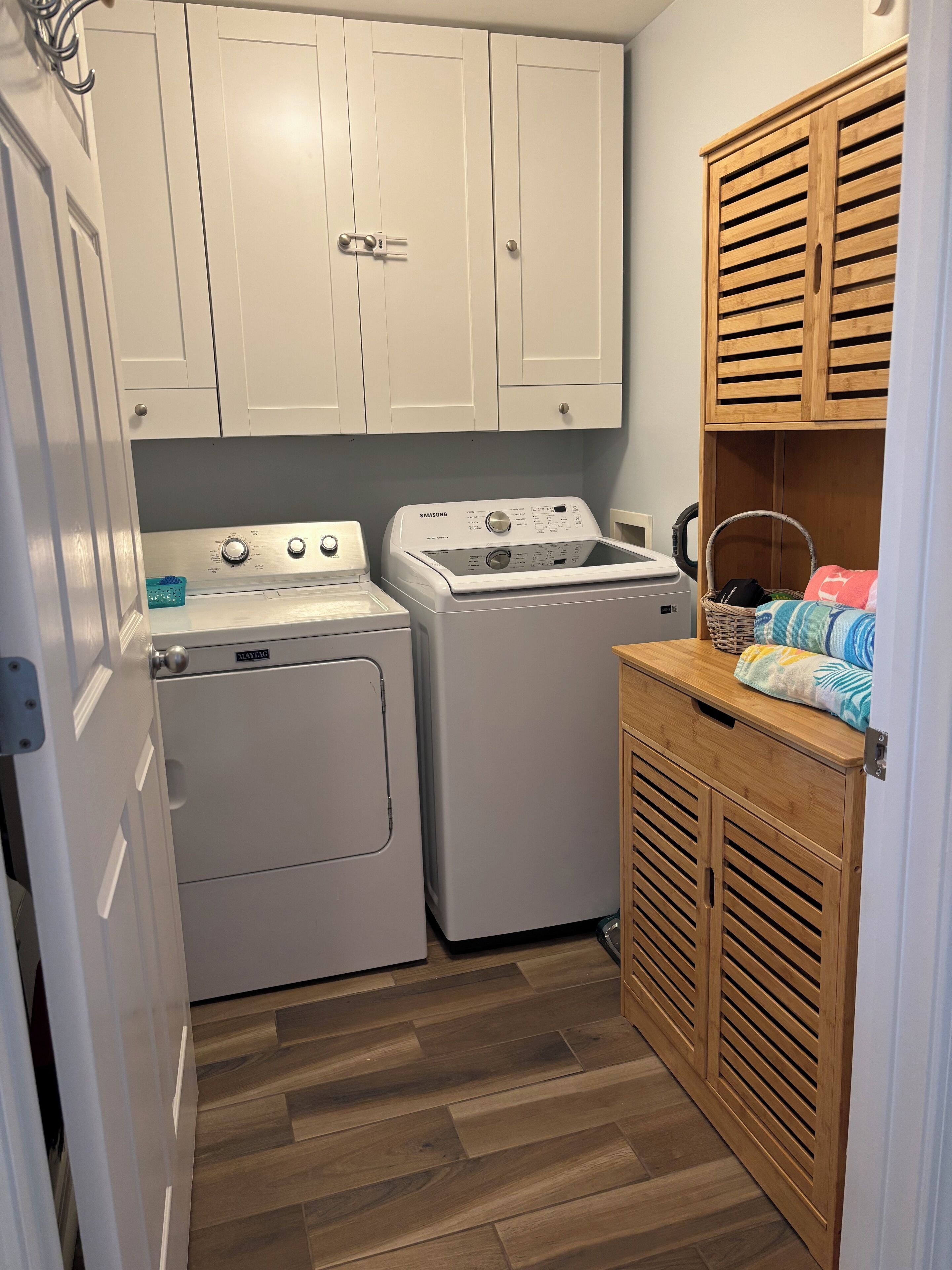 A laundry room with two white washing machines, a drying machine, and a wooden cabinet with a basket.