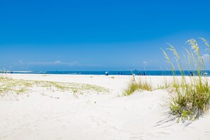 Una playa con arena blanca, cielo azul despejado y océano al fondo.