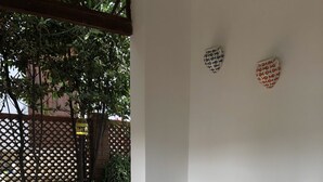 Mesa de madeira com bandeja trançada, rodeada por cadeiras de vime, sobre um pátio calçado com vista para vegetação e cerca de madeira.
