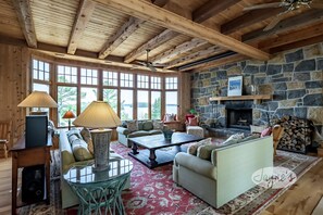 A cozy living room with wooden beams, stone fireplace, and large windows. - Incredible 9 bdrm, 9 bath, Tennis Court! Nanny Suite! Gym! Lake Muskoka!!! (Port Carling)