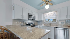 A kitchen with white cabinets, a granite countertop, stainless steel appliances, and a ceiling fan. - Beach Walk 18 Cozy Condo-Walk to Hangout Festival - Private Pool, Free Parking (Gulf Shores)