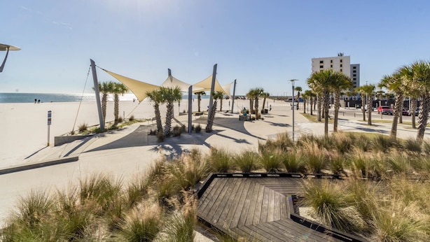 A beachside promenade with a wooden boardwalk, palm trees, and beach umbrellas. - Beach Walk 18 Cozy Condo-Walk to Hangout Festival - Private Pool, Free Parking (Gulf Shores)