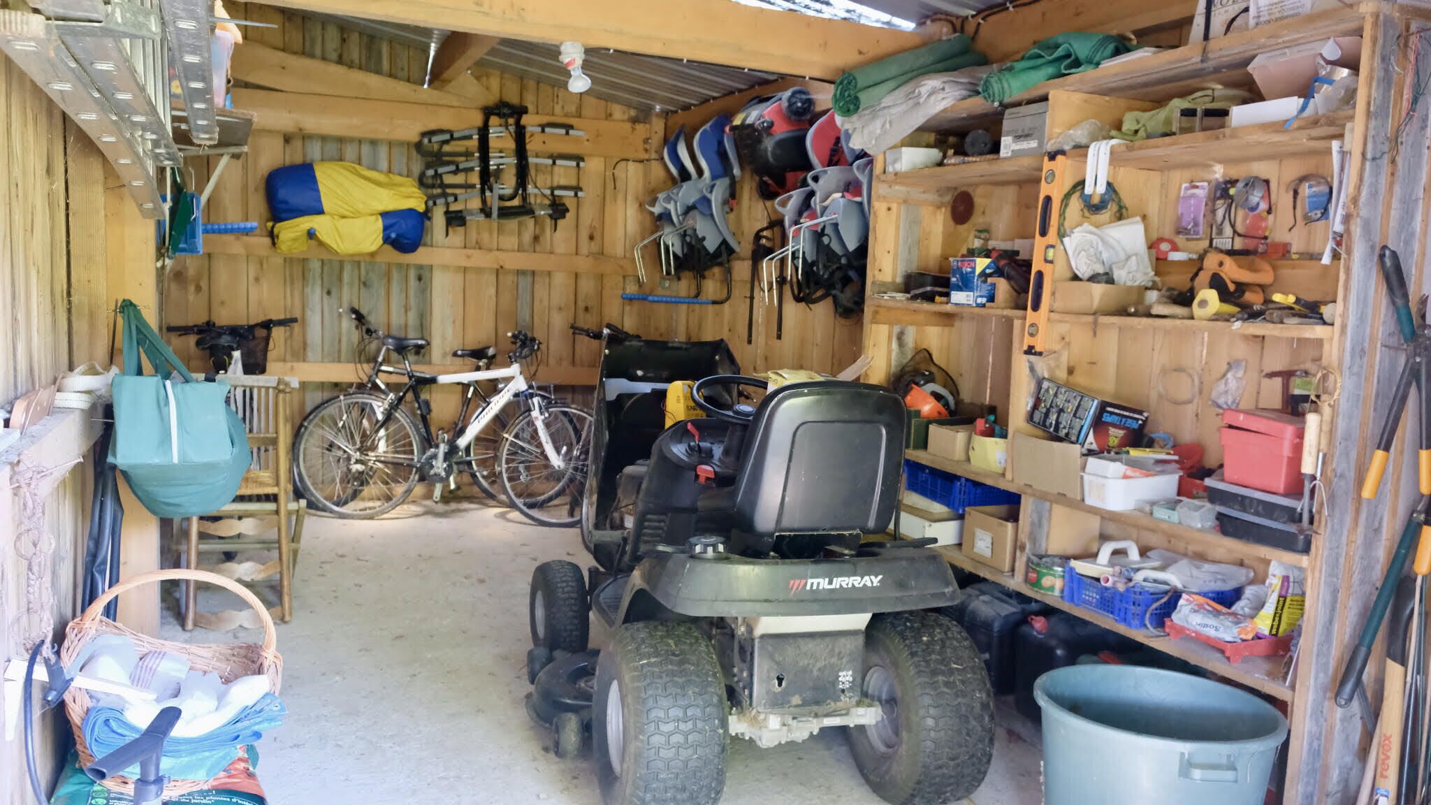 A garage with a lawnmower, a bicycle, and various tools and equipment.
