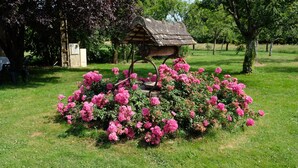 Un jardín con un comedero de pájaros de madera rodeado de flores rosadas.
