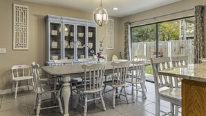 Un comedor con una mesa grande y sillas, un aparador decorativo y vistas a través de un ventanal.
