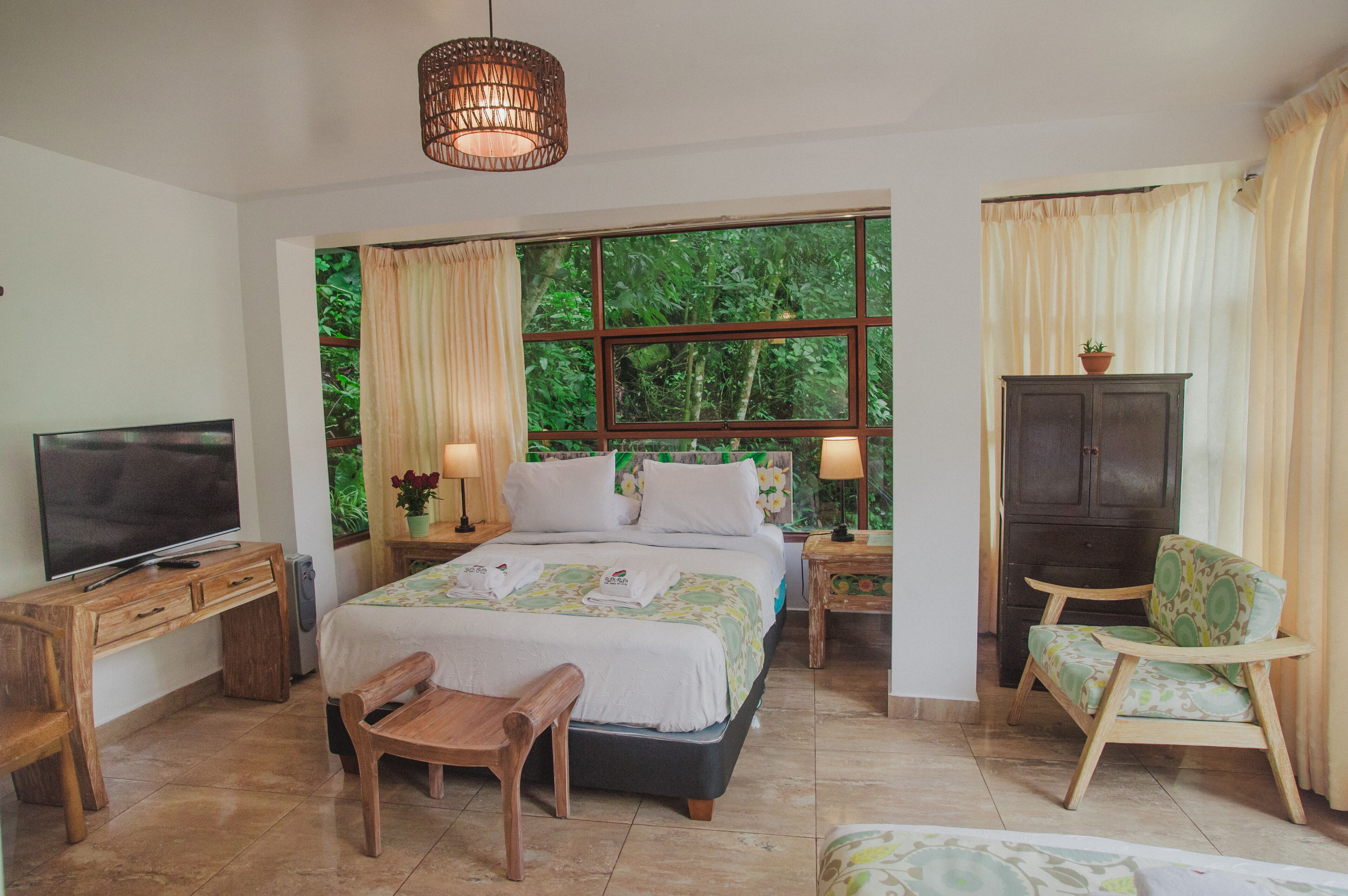 A bedroom with a large bed, a TV, wooden furniture, and a window with curtains.
