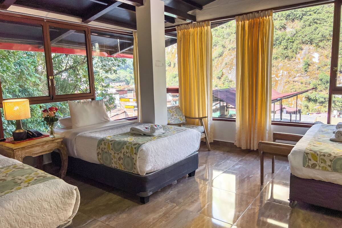 A hotel room with a bed, a bedside table with a lamp, and a view of the outdoors.